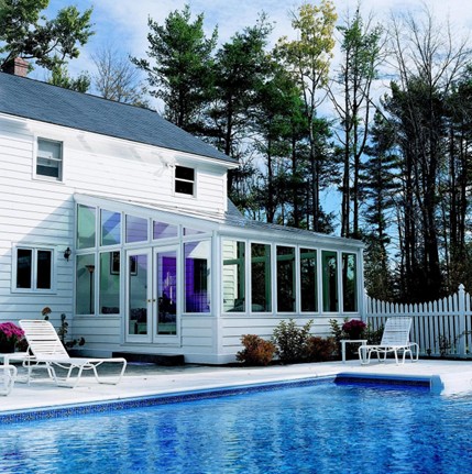 A sunroom overlooking a swimming pool with two white patio chairs